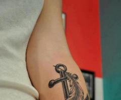 Ancla en sombras con una pluma en antebrazo